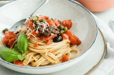 Spaghetti alla Puttanesca in a white bowl with a silver fork.