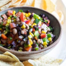 Cowboy caviar in a bowl on a white plate with tortilla chips.