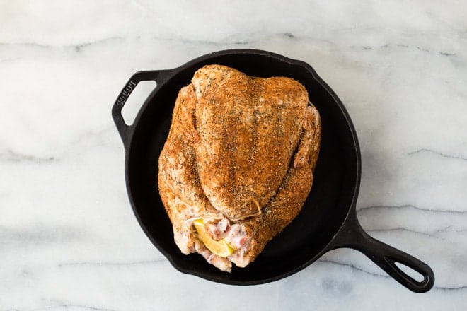 A raw chicken rubbed with seasoning in a cast iron skillet.
