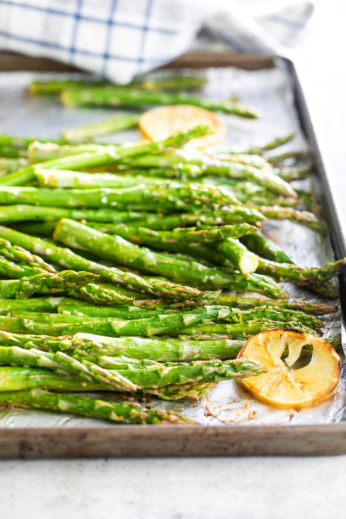 Roasted asparagus on a rimmed baking sheet with lemon slices.