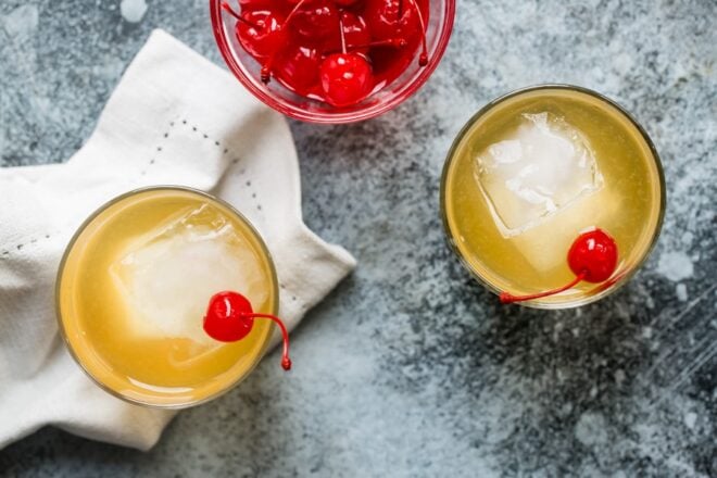 An overhead shot of two whiskey sour cocktails garnished with cherries.