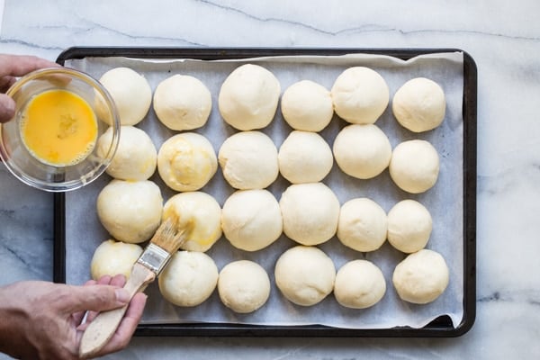 An overhead shot of 20 unbaked soft yeast dinner rolls on a baking sheet.