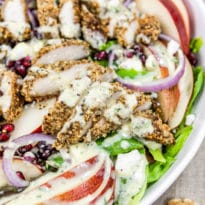 Walnut crusted chicken on a salad in a white bowl.