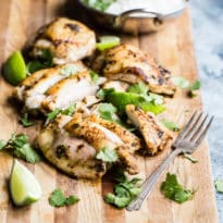 Slices of cilantro lime chicken on a wooden cutting board.