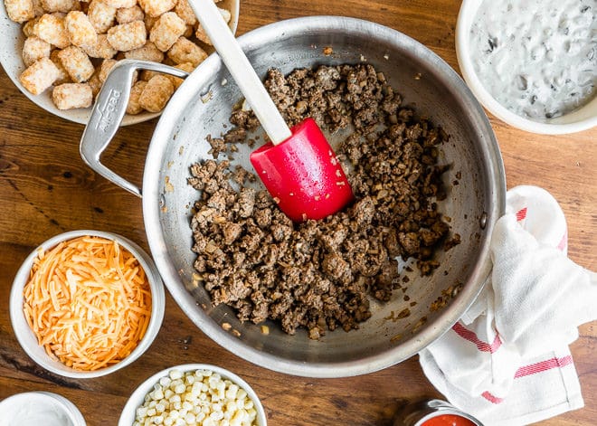 Ground beef in a bowl surrounded by other cowboy casserole toppings.