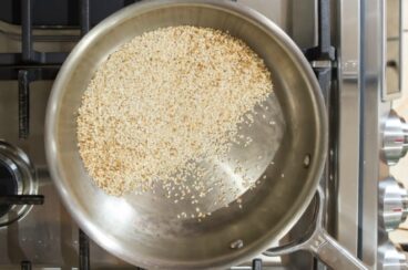 Sesame seeds being toasted in a silver pot on a gas range.