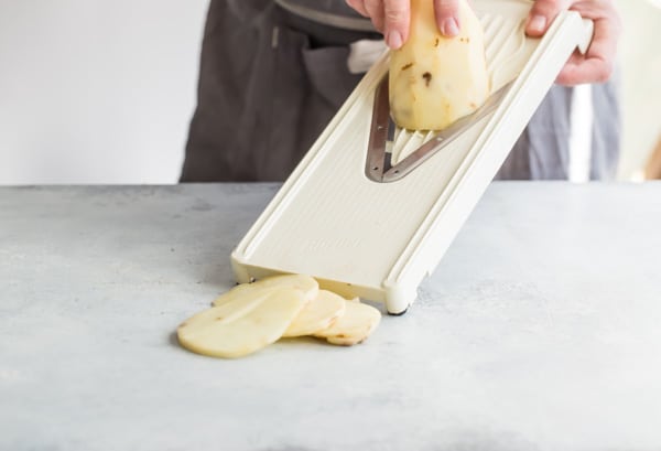 Potatoes being sliced on a mandolin.