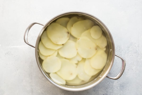 A stock pot full of potato slices, water, and vinegar before boiling.