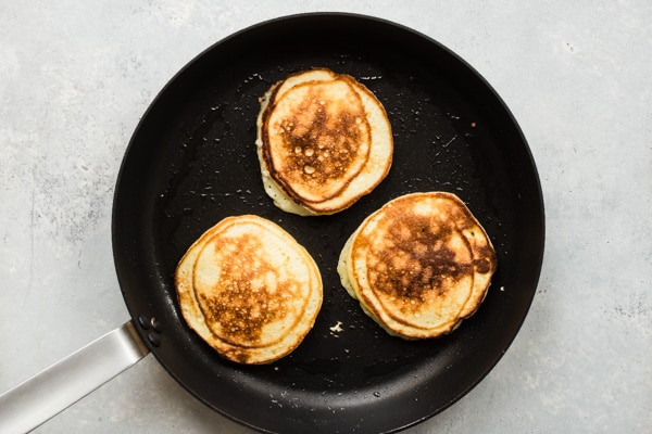 A skillet with 3 lemon ricotta pancakes in it.