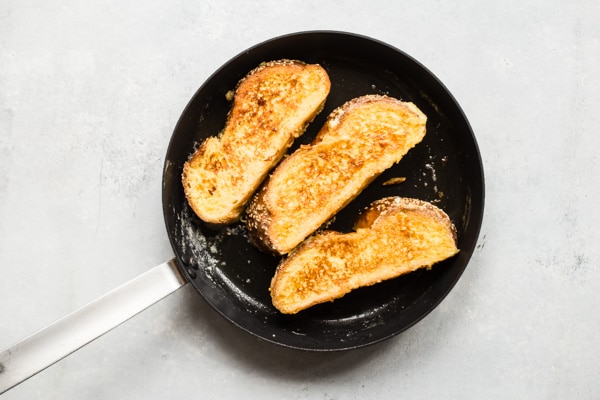 An overhead shot of challah french toast slices in a black skillet.