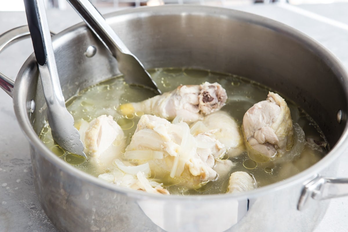 Chicken pieces being poached in water inside a silver pot.