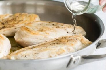 Water being poured into a silver skillet with cooked chicken.