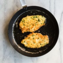 Two pieces of chicken piccata cooking on a black skillet.