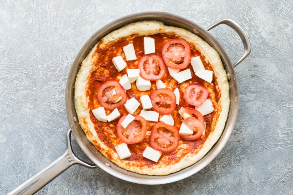 Overhead picture of a margherita pizza in a skillet before being baked.