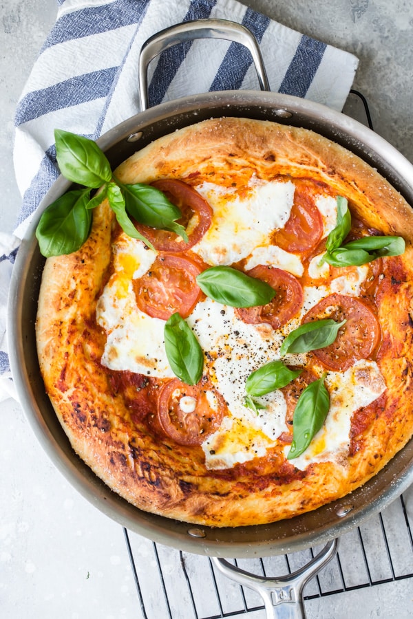 Overhead picture of a margherita pizza in a skillet topped with fresh basil after being baked.