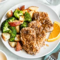 Walnut crusted pork tenderloin with orange maple glaze with broccoli and potatoes on a white plate.