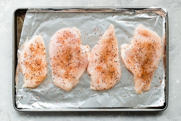 Raw, seasoned chicken breasts on baking pan.