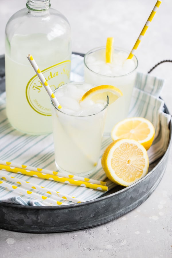 An angled shot of how to make lemonade in glasses in a silver tray.