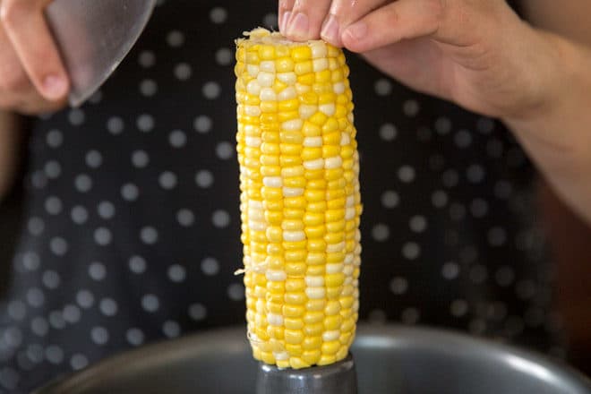A corn cob being held over a cake pan.