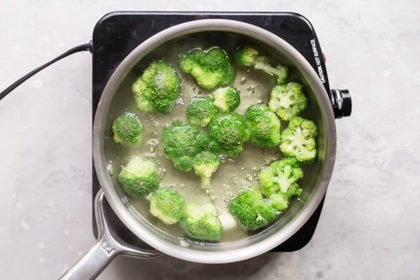 An overhead shot of broccoli boiling in a silver pot.