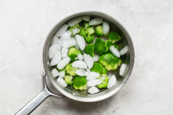 An overhead shot of broccoli in iced water in a silver pot.