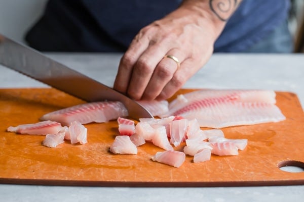A side shot of someone slicing tilapia on a wooden cutting board.