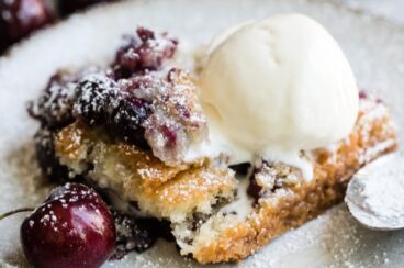 Cherry cobbler topped with ice cream on a white plate.