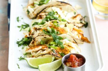 Grilled fish tacos with cabbage slaw on a white serving tray.