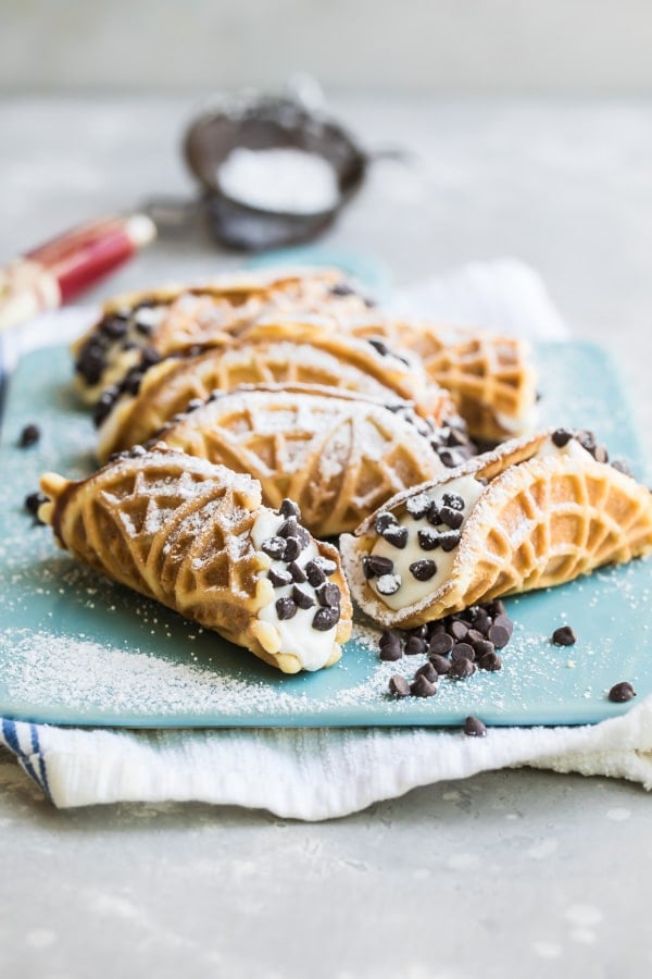 Mock italian cannolis with pizzelle on top of a blue cutting board covered in powdered sugar.