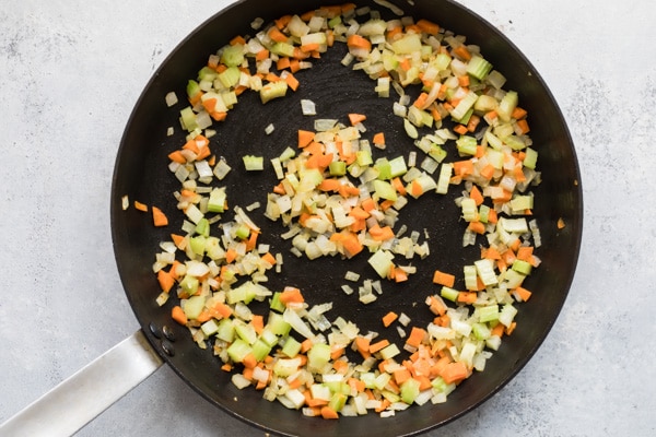 Chopped vegetables cooking in a black skillet.