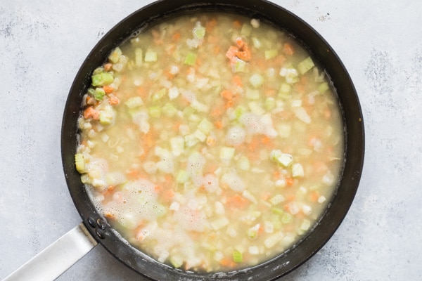 Chopped vegetables and broth cooking in a black skillet.