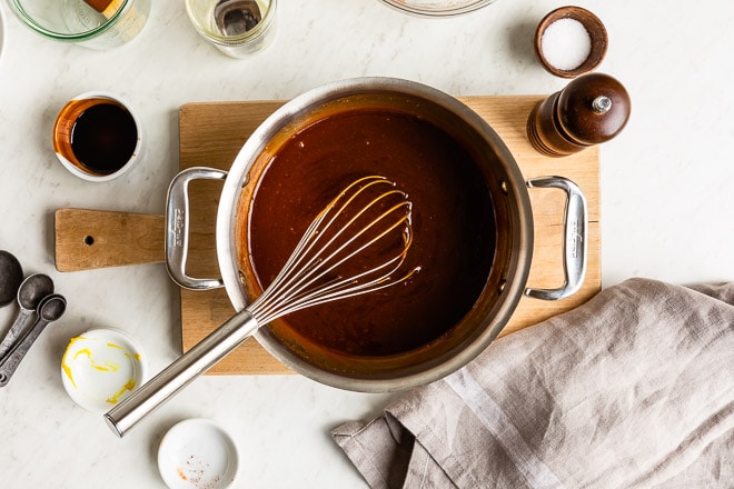 Barbecue sauce in a silver pot with a whisk resting in it.