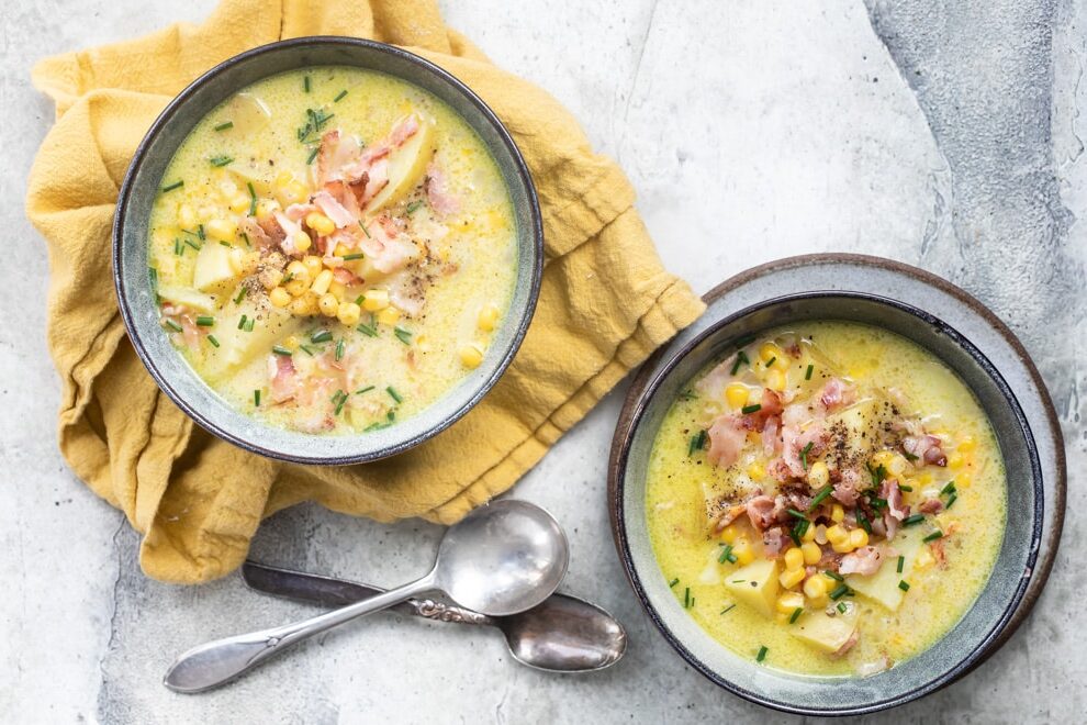 Two bowls of corn chowder on a mustard colored napkin.