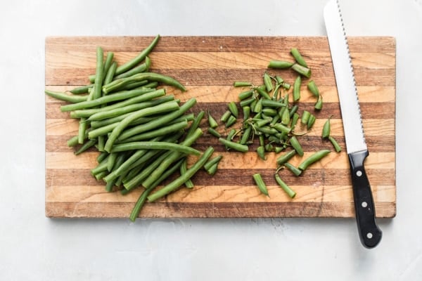 Green beans on a wood cutting board with their ends cut off.