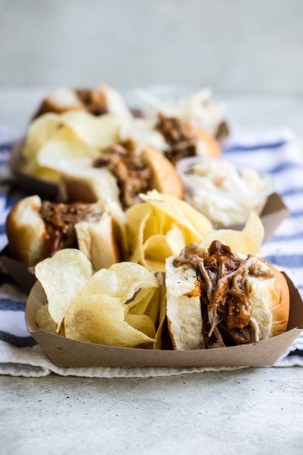 Slow cooker pulled pork sandwiches with chips in brown trays.
