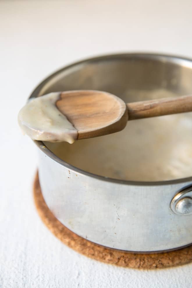 Condensed cream of chicken soup on a wooden spoon resting on a silver pot.