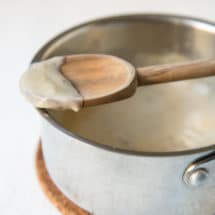 Condensed cream of chicken soup on a wooden spoon resting on a silver pot.
