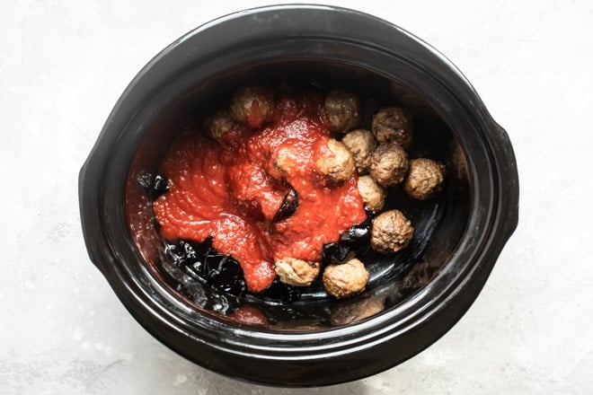 Meatballs, chili sauce, and grape jelly in a black slow cooker.