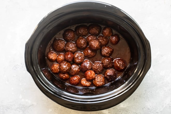 Crockpot meatballs with grape jelly sauce in a black slow cooker.