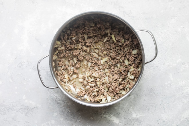 Ground beef and onions cooking in a silver pot.