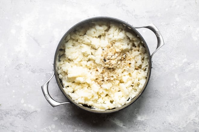 Garlic mashed potatoes and ingredients in a black pot.