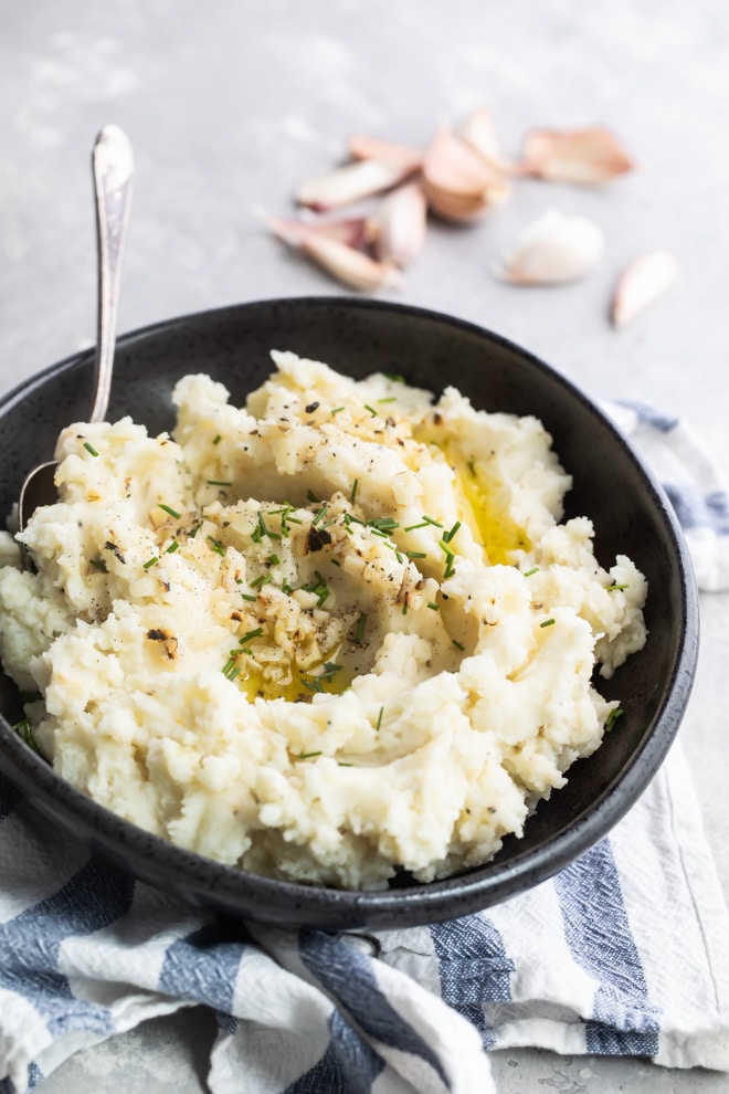 Garlic mashed potatoes in a black bowl with a serving spoon on a blue and white striped towel.