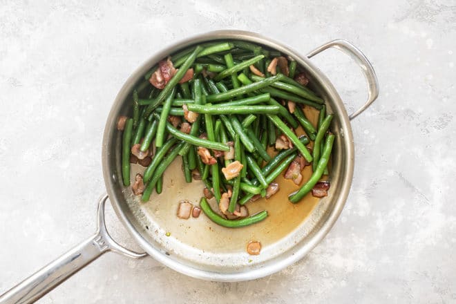 Cooked green beans with bacon in a skillet.