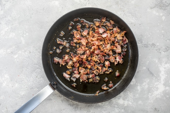 An overhead shot of bacon cooking in a black skillet.