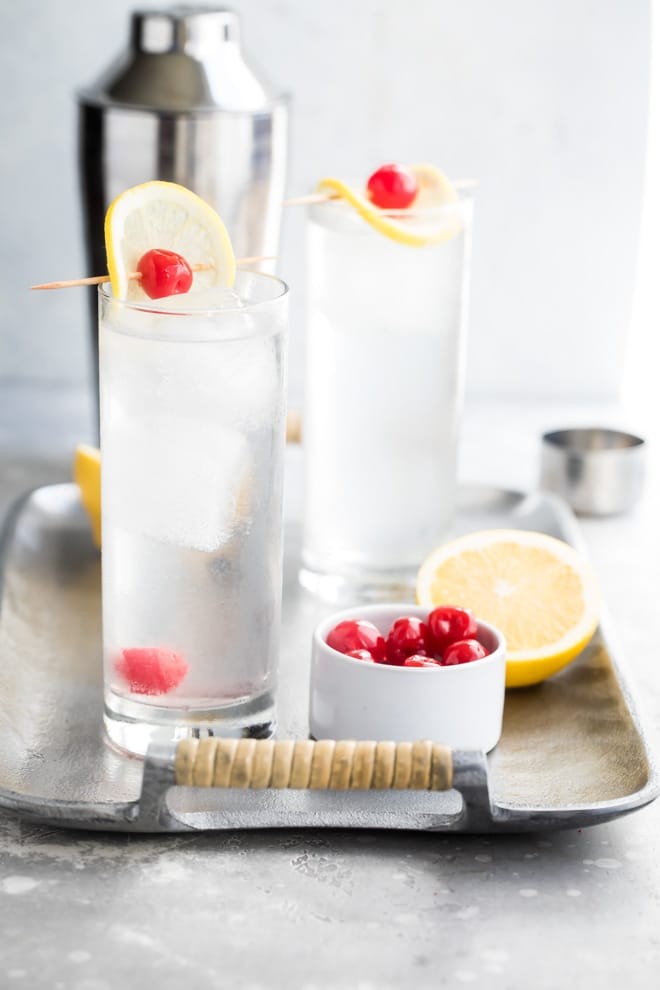 Tom collins in two clear glasses on a silver tray.