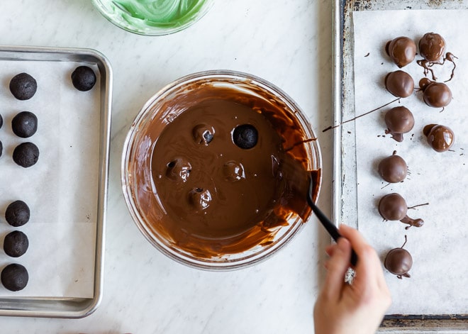 An overhead shot of no bake mint Oreo truffle balls being dipped and coated in melted chocolate.