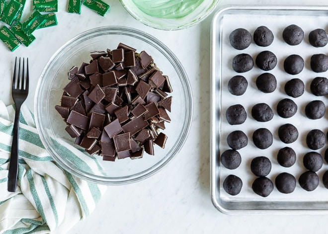 An overhead shot of solid andes mints in a clear bowl and a pan of no bake mint Oreo truffles.