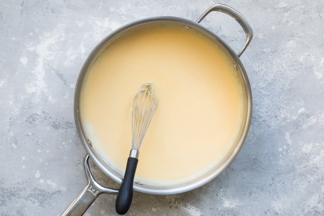 Cheese sauce in a silver skillet with a whisk.