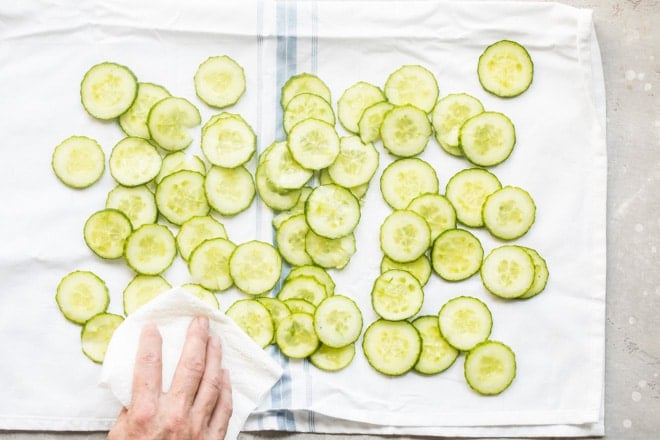 Sliced cucumbers being dried on a white towel.