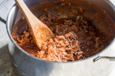 Homemade meat sauce in a silver pot with a wooden spoon.
